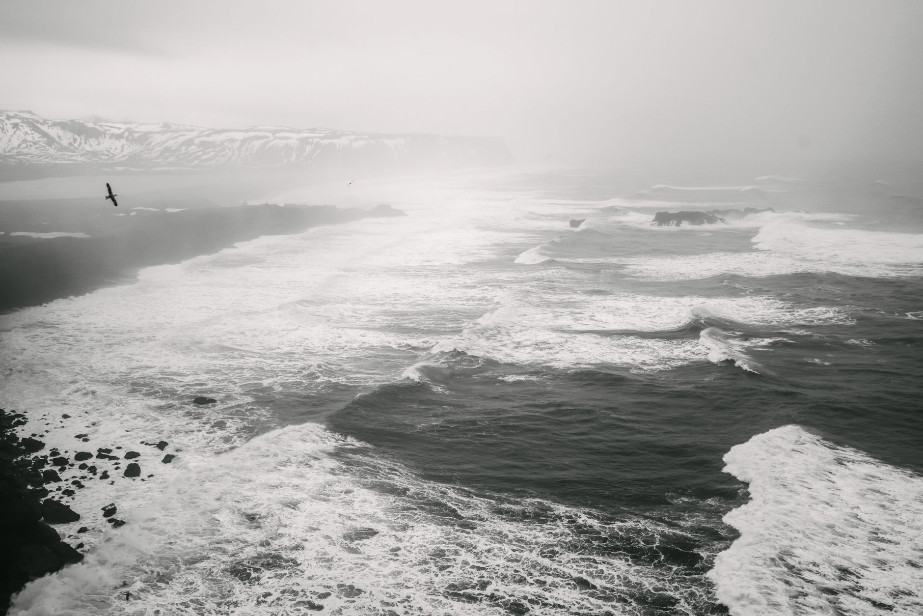 Moody foggy coastal landscape with crashing ocean waves and distant mountains.
