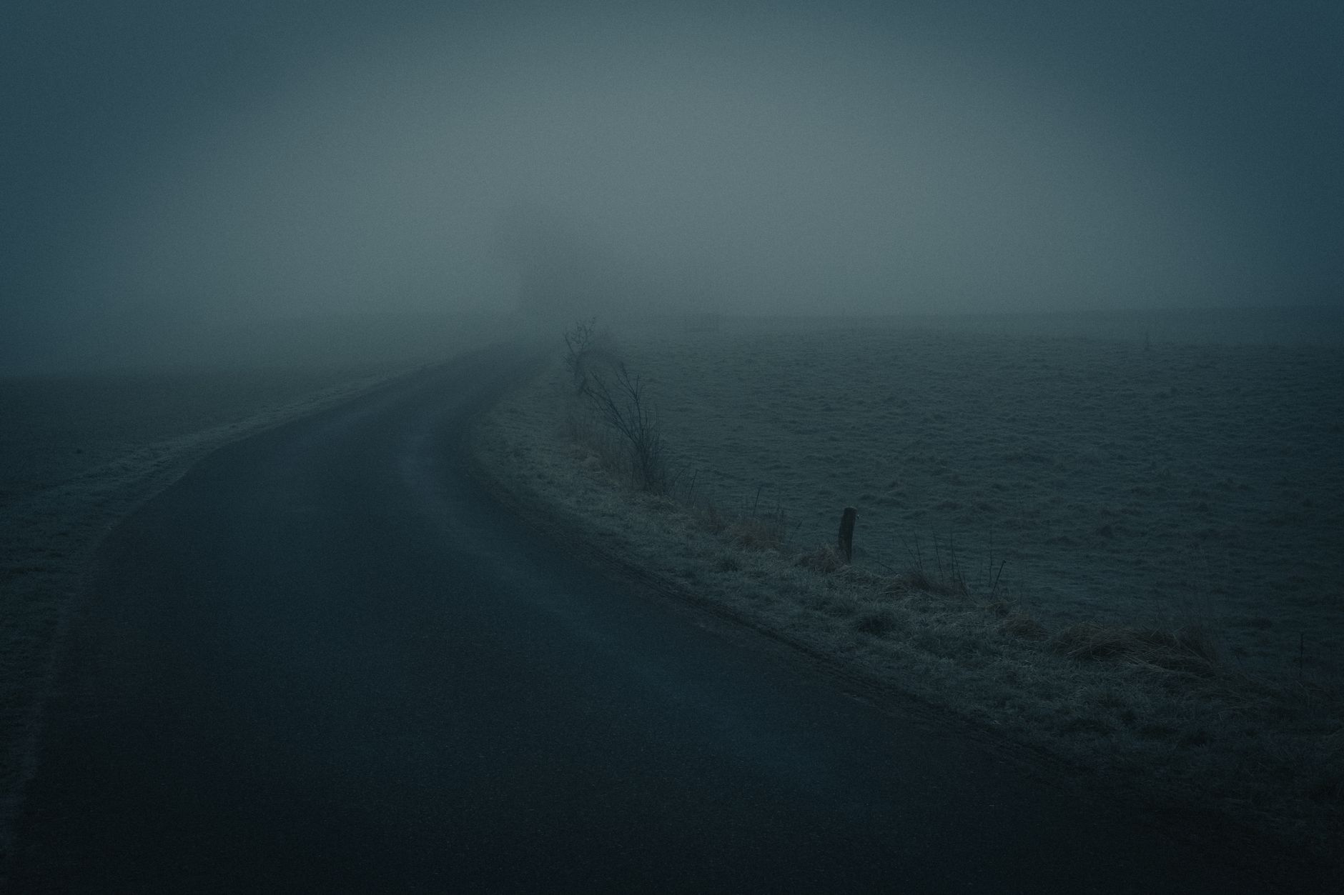 A dark, foggy road in the countryside creates an eerie and mysterious atmosphere.