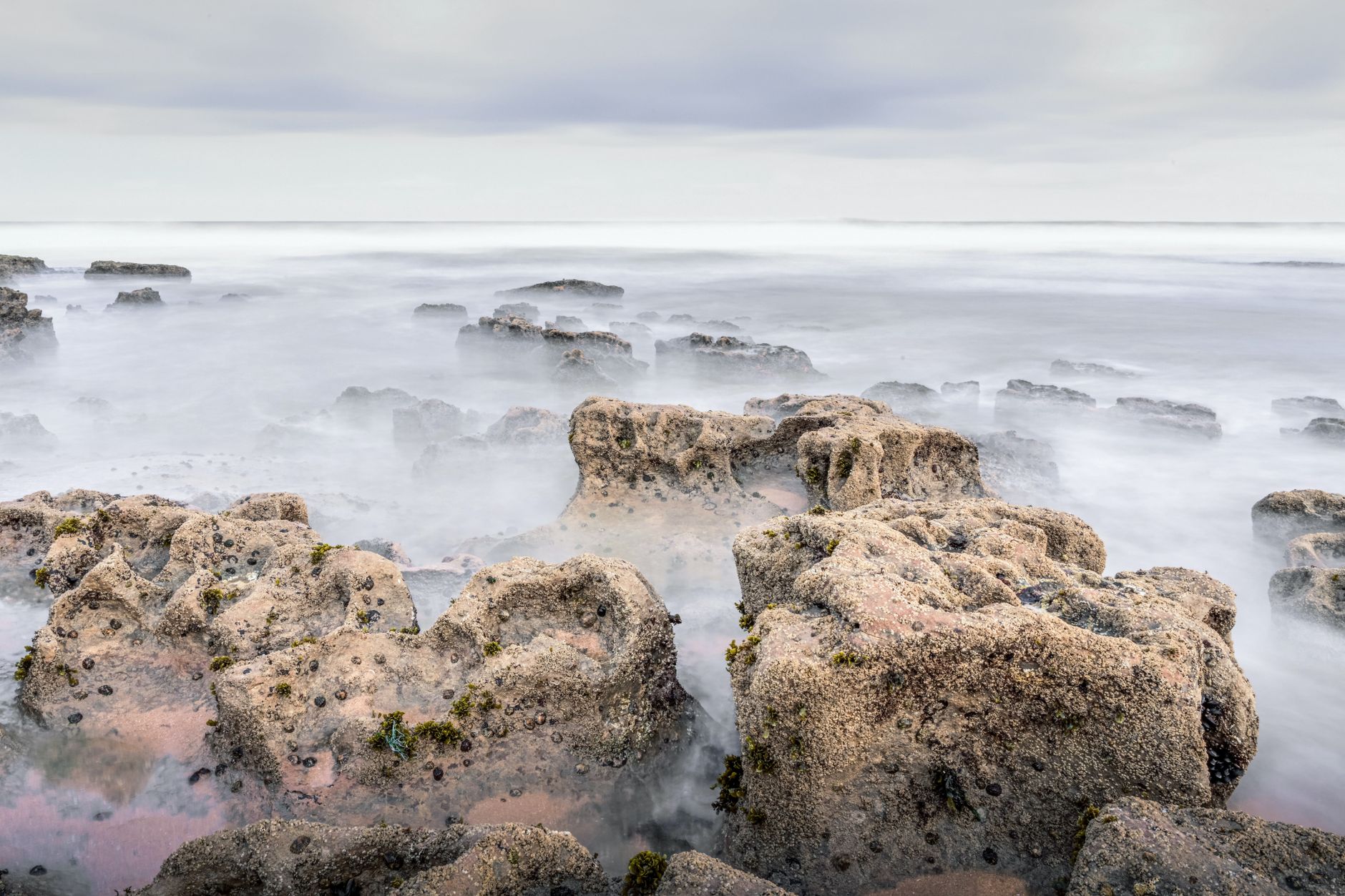 Foggy view of rocky coastline at Ericeira, Portugal, with misty sea and overcast sky.