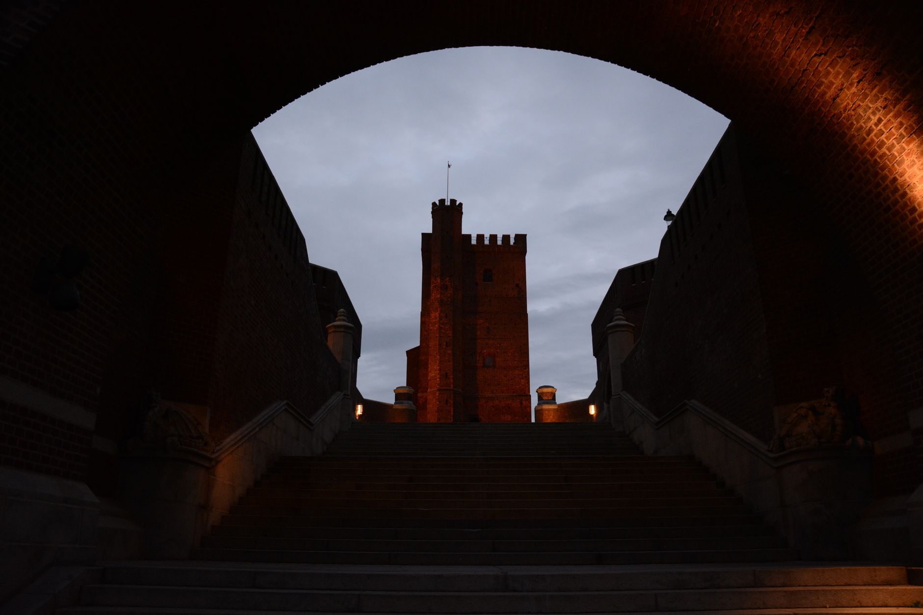 A grand view of a historic castle through an archway, beautifully lit at twilight.