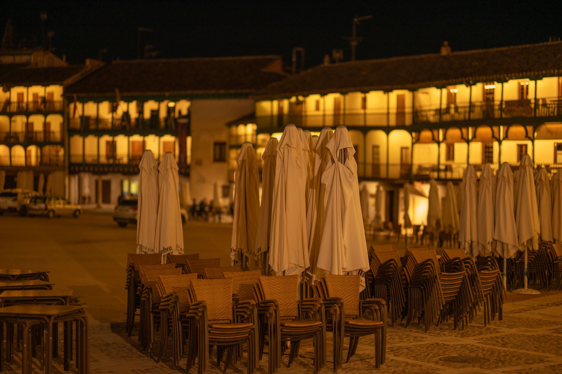 Night view of the historic Plaza Mayor in Chinchón, Spain with stacked chairs and closed umbrellas.