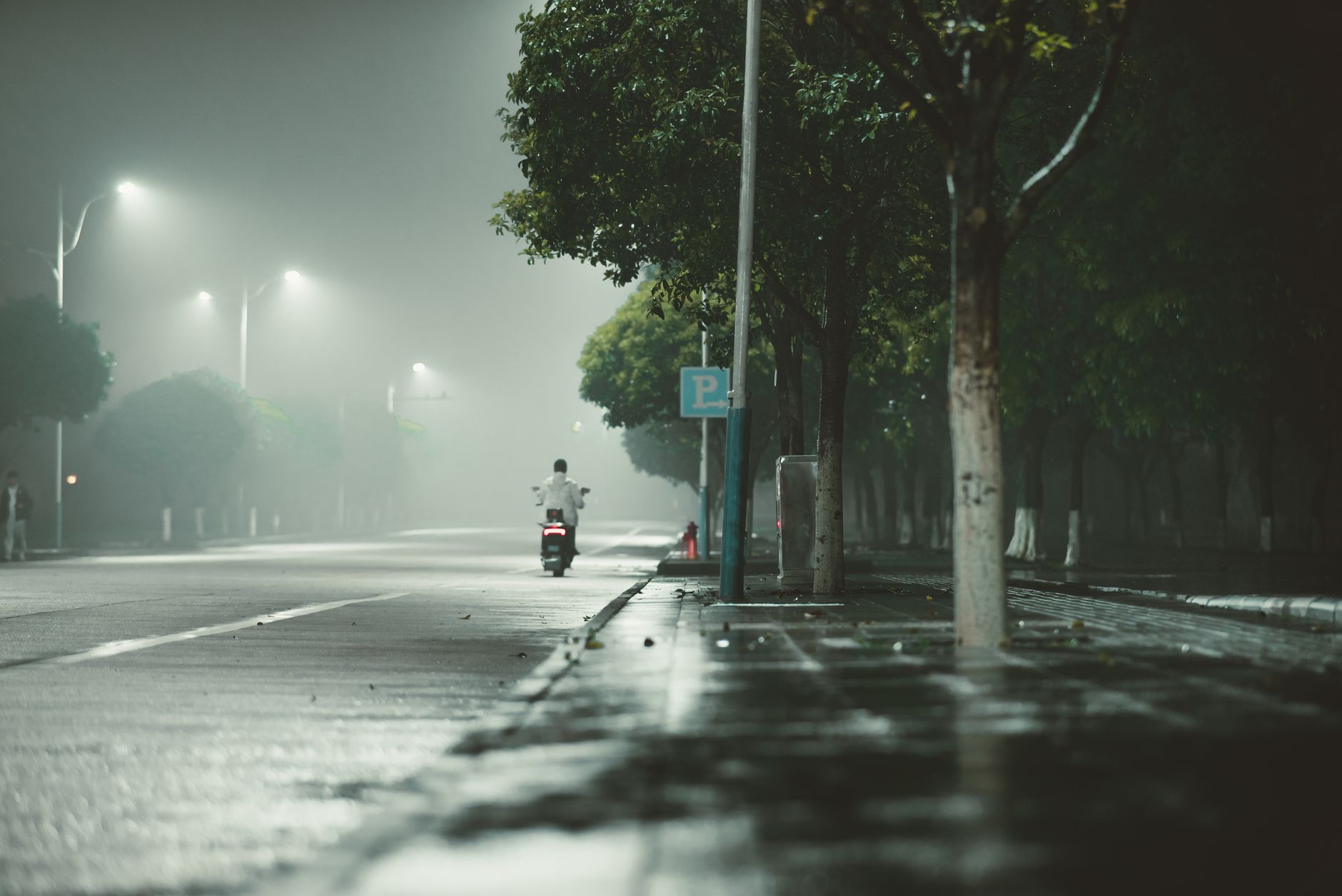 A serene, foggy night with a lone motorcyclist on an empty street under streetlights.
