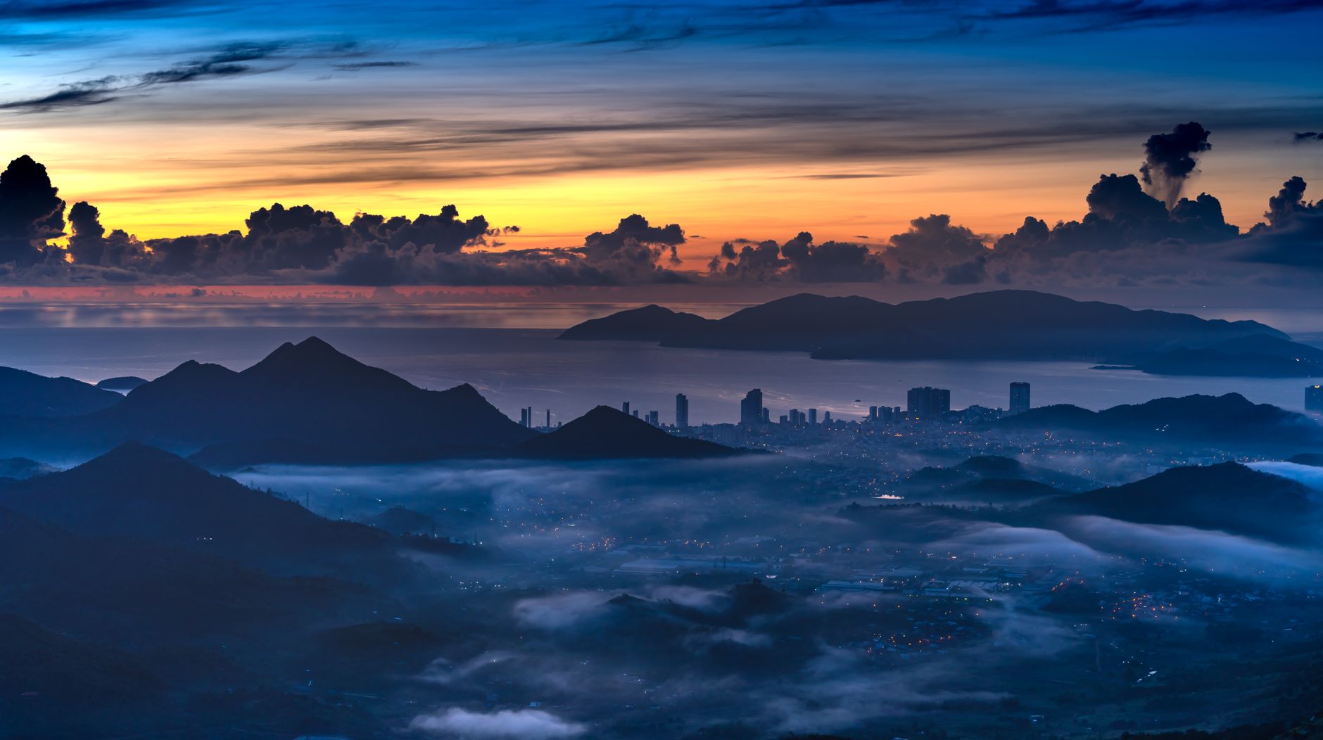 A breathtaking twilight cityscape with illuminated urban skyline, mountains, and clouds.