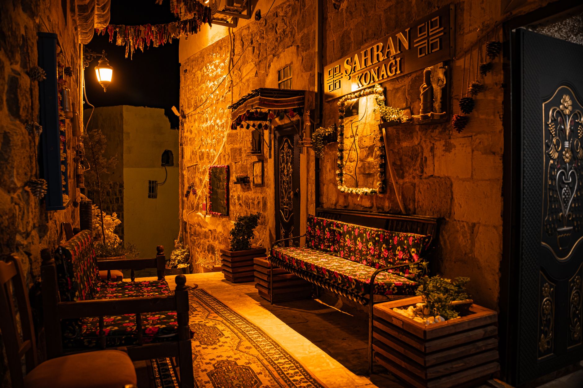 Warmly lit stone street in Mardin, Türkiye with decorative seating and traditional architecture at night.